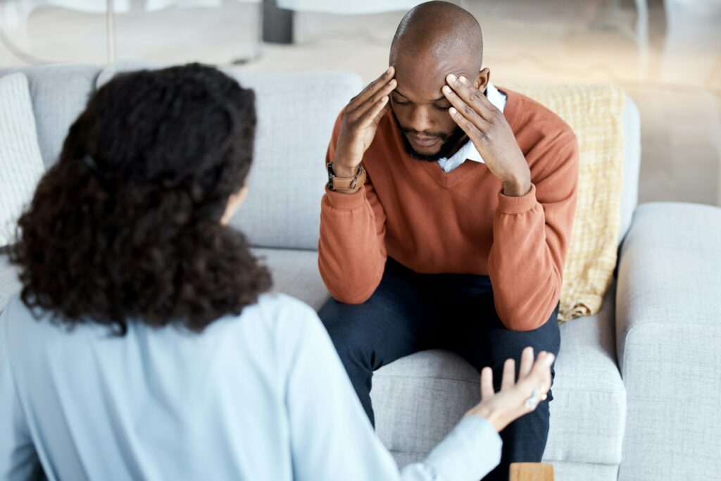 Black man, mental health and counseling with woman psychologist, stress headache and depression wit